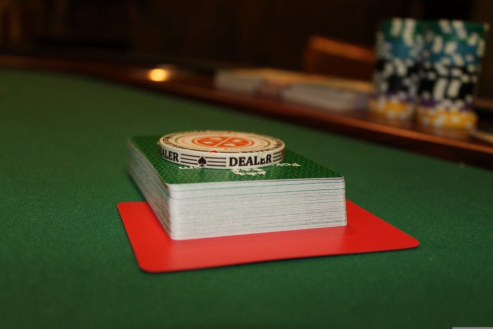 Un botón de dealer y un mazo de cartas sobre una mesa de poker verde vacía