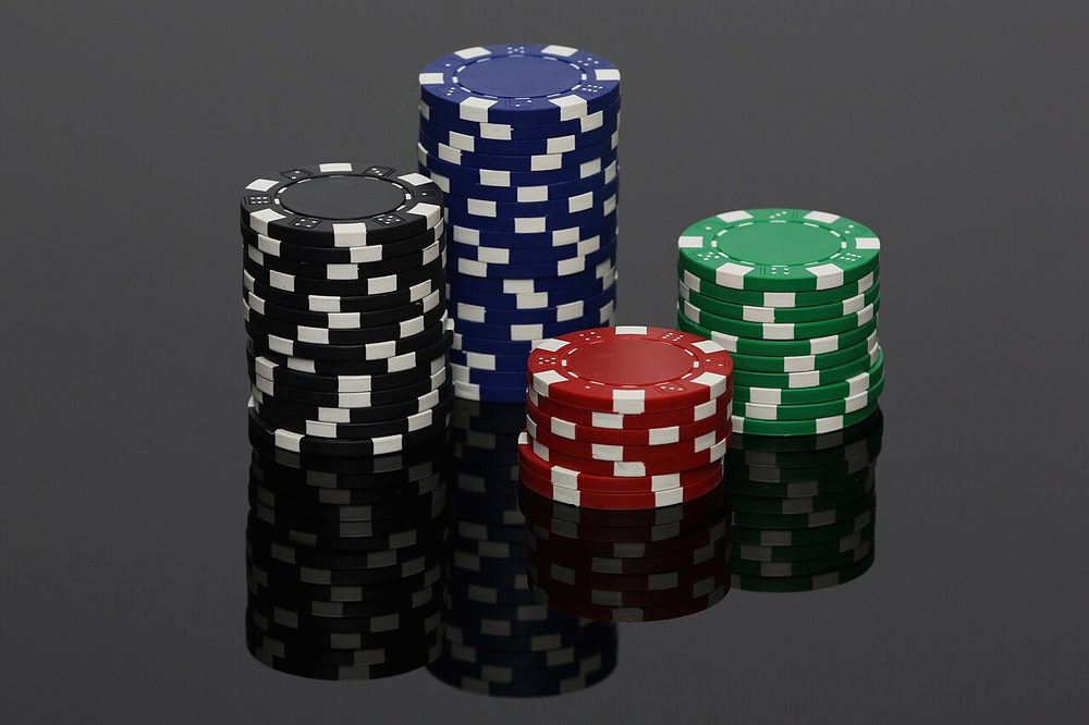 Cuatro torres de fichas de poker reflejadas sobre una superficie oscura