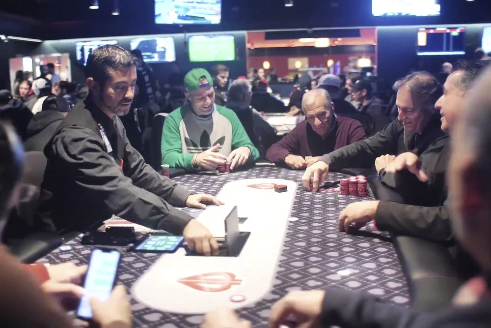 Jugadores sentados alrededor de una mesa de poker en una sala de torneo concurrida